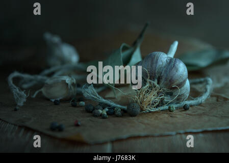 Kopf Knoblauch, Knoblauchzehen, Lorbeerblätter auf einem Holzbrett auf dunklem Hintergrund Stockfoto