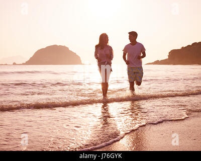 junge asiatische Brautpaar in den frühen Morgenstunden am Strand laufen.