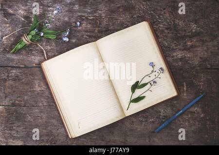 Auf einem alten hölzernen Hintergrund liegt ein altes Notizbuch und ein Blumenstrauß blaue Vergissmeinnicht, eine Ansicht von oben. Das Konzept der Romantik, Einfachheit, Tagebuch schreiben. Stockfoto