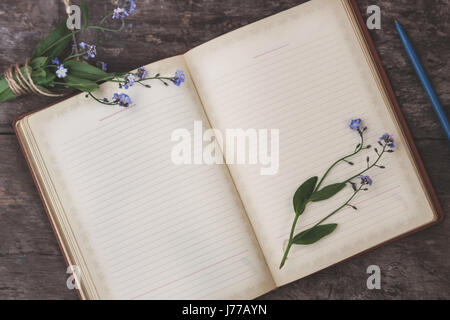 Auf einem alten hölzernen Hintergrund liegt ein altes Notizbuch und ein Blumenstrauß blaue Vergissmeinnicht, eine Ansicht von oben. Das Konzept der Romantik, Einfachheit, Tagebuch schreiben. Stockfoto