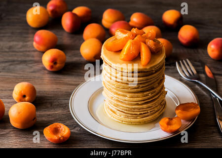 Stapel von hausgemachte amerikanische Pfannkuchen serviert mit Honig und Aprikosen auf hölzernen Hintergrund. Stockfoto