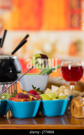 Köstliche Kiwi in einem Metallstab mit verschiedenen frischen Früchten im inneren Schalen mit Rotwein in eine Tasse auf Holztisch Stockfoto