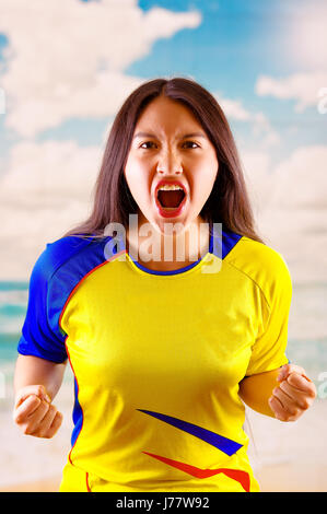 Jungen ecuadorianischen Frau mit offiziellen Marathon Fußball Shirt stehen vor der Kamera, sehr engagierte Körpersprache beobachten Spiel mit großer Begeisterung, blauer Himmel und Wolken-Hintergrund Stockfoto