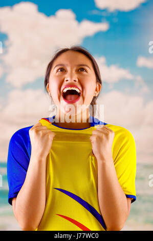 Jungen ecuadorianischen Frau mit offiziellen Marathon Fußball Shirt stehen vor der Kamera, sehr engagierte Körpersprache beobachten Spiel mit großer Begeisterung, blauer Himmel und Wolken-Hintergrund Stockfoto