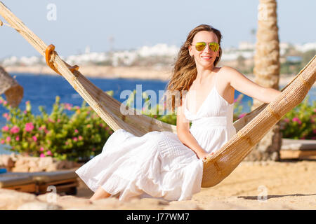 Junge schöne Frau im weißen Kleid zum Entspannen in der Hängematte in der Nähe der Küste. Sommer Urlaub Hintergrund Stockfoto