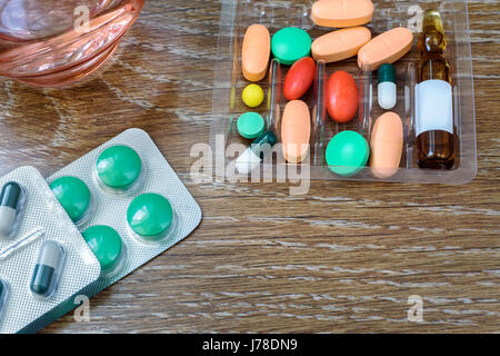 Auf dem Tisch liegen verschiedene Arten von Pillen und Fläschchen. Neben einem Glas Wasser steht für die Verwendung der Medikamente. Stockfoto