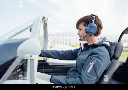 Lächeln Pilotin im Cockpit Leichtflugzeug, sie trägt Flieger Kopfhörer und Kontrollen überprüfen Stockfoto