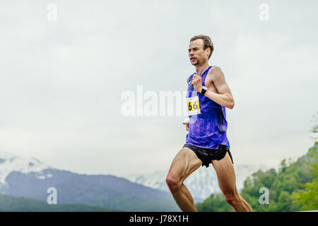 junge männliche Läufer auf Hintergrund Himmel und Berge im Rennen Spring Mountain Marathon laufen Stockfoto