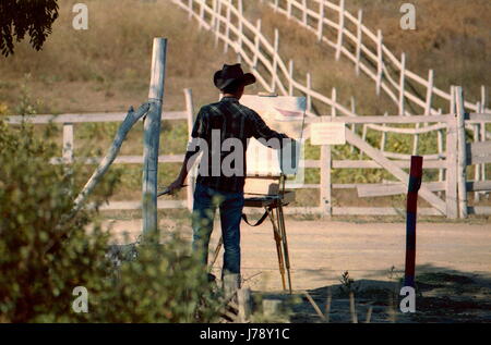 Künstler in Cowboy-Hut malt ein Bild von Öl-Malerei. Draußen, in der Nähe der Ranch Farm.