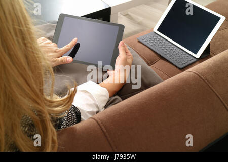 Brünette Frau mit digitalen Talet und Laptop-Computer auf Sofa im Wohnzimmer Stockfoto