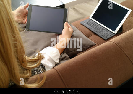 Brünette Frau mit digitalen Talet und Laptop-Computer auf Sofa im Wohnzimmer Stockfoto