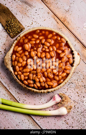 High-Angle Shot eine Steingut-Schale voll Bohnen und einige grüne Knoblauch auf einem rustikalen Holztisch Stockfoto