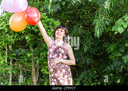 Schwangere Frau mit bunten Luftballons in den Sommerpark. Stockfoto