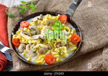 Vegetarische schwäbische Spätzle mit verdickten Sahnesauce und frischen Champignons serviert in einer eisernen Pfanne auf einem rustikalen Tisch mit einer alten Jute-sack Stockfoto