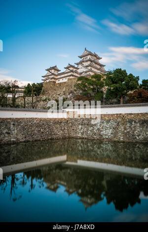 Die Burg Himeji steht auf einem Hügel standhaft und spiegelt sich im Wasser. Stockfoto