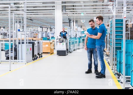 Zwei Männer mit Tablet sprechen in Industriehalle während Mann fahren ein Routenzug Stockfoto