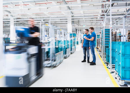 Zwei Männer mit Tablet sprechen in Industriehalle während Mann fahren ein Routenzug Stockfoto