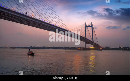 Vidyasagar setu Brücke bei Dämmerung mit einem hölzernen Boot auf dem Fluss Hooghly. Stockfoto