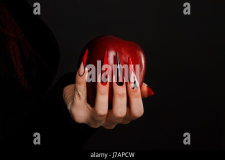 Hände mit beängstigend Nägel Maniküre hält vergifteten Apfel roten Stockfoto