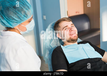 Porträt des Mannes. Lächeln Sie Gesicht. Zahnärztliche Versorgung Konzept. Zahnärztliche Untersuchung wird schöner Mann umgeben von Zahnarzt eingeräumt. Stockfoto