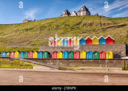 Reihen von bunten Strandhäuschen auf der Promenade bei Whitby Sands, Whitby, North Yorkshire, England, UK, an einem schönen sonnigen Morgen im Frühling. Stockfoto