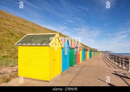 Bunte Strandhäuschen entlang der Promenade am Nordstrand, Whitby, North Yorkshire, England, UK, früh an einem hellen sonnigen Frühlingsmorgen. Stockfoto