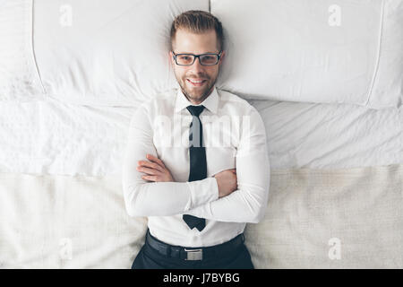 Ansicht von oben. Junge hübsche Geschäftsmann mit Brille auf dem Bett liegend Stockfoto