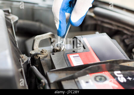 Die Hände des Kfz-Mechaniker in Einweg-Handschuhe Schrauben Sie die Batterie-Kupplung. Die Hand eines Mechanikers mit einem flachen Schlüssel schraubt die Batterie im Auto. Stockfoto