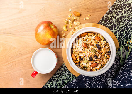 Morgens Müsli in eine Schüssel mit voller Apple und Tasse Milch auf Holztisch mit asiatischen Stil Serviette, Seite warmen Morgenlicht, Raum für Textfreiraum Stockfoto