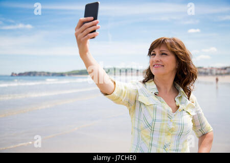Schöne mittlere gealterte Frau machen eine Selfie am Strand Stockfoto
