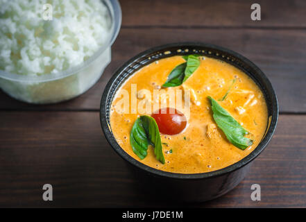 eine Schüssel mit Fisch-Curry mit Basilikum-Blätter und eine Schüssel mit gekochtem Reis auf einem Holztisch Stockfoto