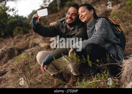 Liebespaar auf Bergweg und nehmen Selfie sitzen. Junger Mann und Frau in Landschaft wandern und Selbstbildnis mit Handy sprechen. Stockfoto