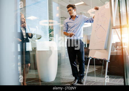 Büroangestellte in der Nähe von Flip-Chart mit Diagramm stehen. Reife Geschäftsmann hält einen Vortrag auf einem Flipchart an Kollegen. Stockfoto