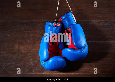Ein paar helle blaue und rote Boxhandschuhe hängt hölzernen Hintergrund. Boxen-Hintergründe und Stillleben. Farbenfrohe Accessoires für den Sport. Horizo Stockfoto