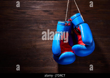 Ein paar helle blaue und rote Boxhandschuhe hängt hölzernen Hintergrund. Boxen-Hintergründe und Stillleben. Farbenfrohe Accessoires für den Sport. Horizo Stockfoto