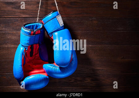 Ein paar helle blaue und rote Boxhandschuhe hängt hölzernen Hintergrund. Boxen-Hintergründe und Stillleben. Farbenfrohe Accessoires für den Sport. Horizo Stockfoto