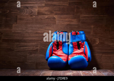 Boxen-Hintergrund mit zwei Handschuhe auf dem braunen Plank-Hintergrund. Horizontale Foto von blauen und roten Boxhandschuhe gegen Holzwand. Boxen-traini Stockfoto