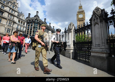 Ein Mitglied der Armee trifft sich vor den Houses of Parliament in London zu Polizeibeamten, nachdem Scotland Yard angekündigt hatte, dass bewaffnete Truppen eingesetzt werden, um wichtige Orte wie den Buckingham Palace, die Downing Street, den Palace of Westminster und Botschaften zu bewachen. Stockfoto