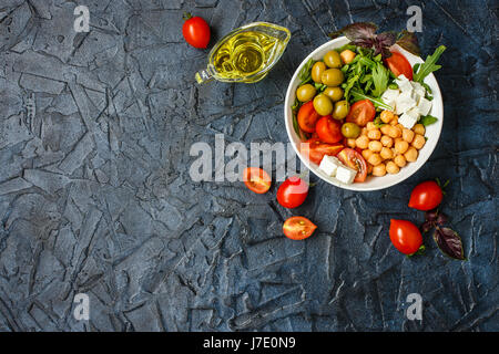 Vegetarisches Buddha Schüssel mit Kichererbsen, Rucola, Cherry-Tomaten, Feta-Käse und Oliven. Olivenöl, Tomaten auf Tisch, gesunde Ernährung. Ansicht von oben. P Stockfoto