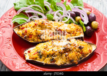 Auberginen gefüllt mit Couscous mit frischem Salat und Oliven auf der roten Platte serviert. Stockfoto