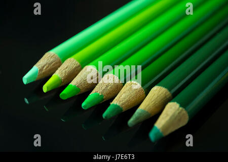 Sieben grüne Bleistifte verschiedener Farbtöne und Schattierungen, aufgereiht von hell bis dunkel auf einer schwarzen reflektierenden Oberfläche. Stockfoto