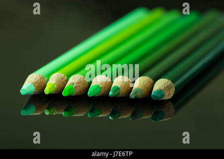 Sieben grüne Bleistifte verschiedener Farbtöne und Schattierungen, aufgereiht von hell bis dunkel auf einer schwarzen reflektierenden Oberfläche. Stockfoto