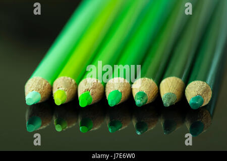 Sieben grüne Bleistifte verschiedener Farbtöne und Schattierungen, aufgereiht von hell bis dunkel auf einer schwarzen reflektierenden Oberfläche. Stockfoto