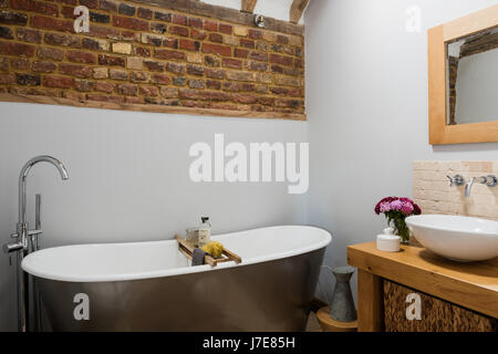 Freistehende Badewanne im rustikalen Badezimmer mit freiliegenden Ziegelwand. Die Wände sind von Albany in hellgrau lackiert. Stockfoto