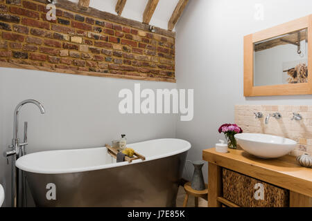 Freistehende Badewanne im rustikalen Badezimmer mit freiliegenden Ziegelwand. Die Wände sind von Albany in hellgrau lackiert. Stockfoto