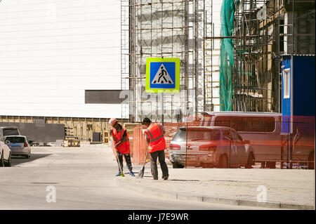 Arbeiter im Overall fegt Gehweg mit einem Besen auf Stadtstraße an warmen Sommertag Stockfoto