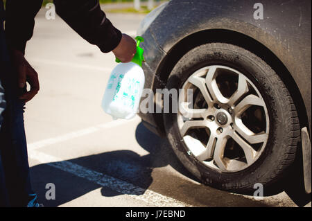 junge bärtiger Mann wäscht sein Auto Felgen, Spritzwasser von Spray, in Parken an der Straße Stockfoto