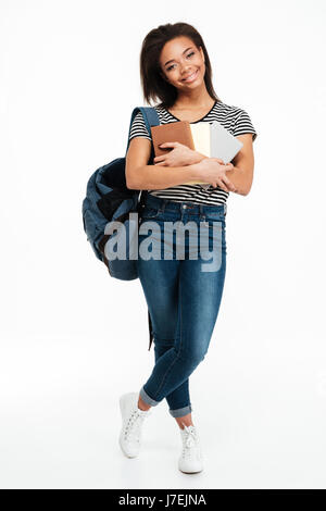 In voller Länge Portrait von ein Lächeln auf den Lippen afrikanischer Teenager Mädchen Rucksack trägt und hält Bücher isoliert auf weißem Hintergrund Stockfoto