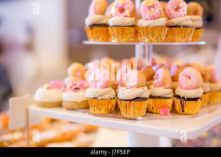 Mini Schokoladen Cupcakes mit Mini rosa Donuts auf einem Desserttisch gekrönt. Sie werden auf einem Tablett gestuften Anzeige angezeigt. Stockfoto