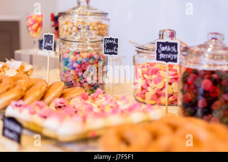 Bunte Bonbons in Gläsern auf einem Desserttisch mit Donuts, Cookies und Popcorn. Es gibt süße Tafel Zeichen. Stockfoto